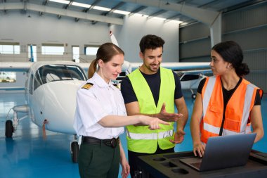 Havacılık uzmanları uçak bakımı konusunda işbirliği yapıyorlar. Bir uçak hangarında teşhis ve planlama için dizüstü bilgisayar kullanıyorlar.