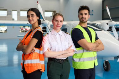 Bir pilot ve tamirci de dahil olmak üzere kendinden emin havacılık uzmanları hangarda gururla duruyor ve çalışmaya hazırlar.