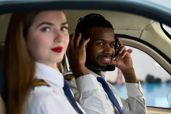 Üniforma giyen ve kulaklık takan iki öğrenci pilot bir uçak simülatörünün kokpitinde eğitim görüyor.