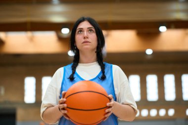 Konsantre basketbol oyuncusu topu tutuyor, spor salonundaki hedefe odaklanıyor, spora olan azmini ve tutkusunu gösteriyor