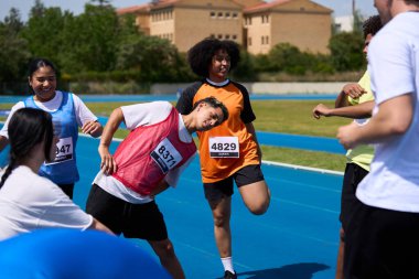 Değişik bir grup sporcu, ilerideki heyecan verici yarışmaya hazırlanan canlı mavi koşu pistinde esniyor ve ısınıyor.