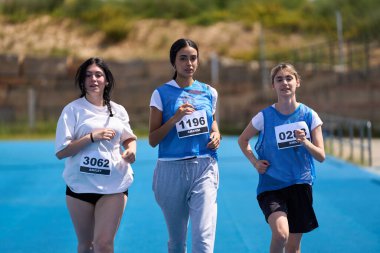 Üç kararlı genç kadın canlı bir mavi pistte bir koşu yarışmasına katılıyor.