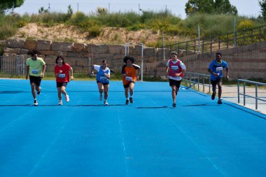 Kararlı atletler canlı mavi bir pistte koşuyor. Yarış sırasında hızlarını ve adanmışlıklarını sergiliyorlar.