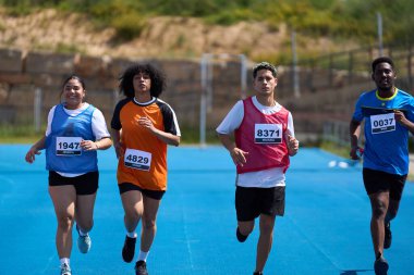 Rekabetçi bir yarışma sırasında dört sporcu, katılımlarını gösteren numaralandırılmış önlükler giyerek canlı mavi bir pistte koşuyor.