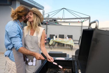 Aşk ve kahkahalarla dolu güzel bir çatı partisinde mangal yaparken öpüşen romantik bir çift.