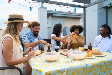 Neşeli çoklu etnik arkadaşlar terasta barbekü partisinin tadını çıkarıyor, birlikte yemek yiyor ve eğleniyorlar.