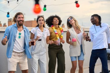 Çeşitli arkadaş grupları çatıda kutlama yapıyor, neşeyle dans ediyor, içkilerini yudumluyor ve birlikte canlı bir yaz akşamının tadını çıkarıyorlar.