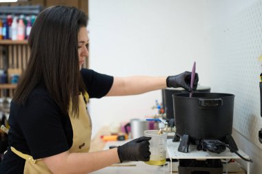 Kadın eritme balmumu, el yapımı mumlar yapmak için araç gereçler ve hazırlık malzemeleri kullanıyor.