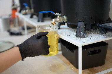 Eldivenli eldiven, cam bir şişeye sıcak balmumu döküyor. Bu da canlı bir stüdyoda mum yapımının sürecini gösteriyor.