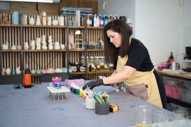 Kadın sanatçı yaratıcı aletlerle dolu renkli ve ilham verici bir stüdyoda el yapımı mumlar yapmak için canlı boyalar hazırlıyor.