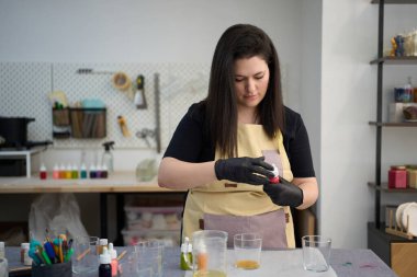 Yoğunlaşmış zanaatkar erimiş balmumuna kırmızı boya ekliyor, canlı stüdyosunda el yapımı mumlar yapıyor.