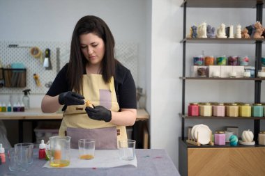 Erimiş balmumuna boya ekleyen usta kadın renkli stüdyosunda el yapımı mumlar yapmaya hazırlanıyor.