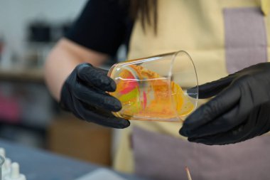 Siyah eldivenler giyen zanaatkar cam bir kavanoza renkli balmumu dökerek eşsiz ve canlı bir el yapımı mum yaratıyor.