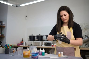 Eldiven giyen usta kadın yaratıcı renkli stüdyosunda el yapımı mumlar yapmak için bir kap hazırlıyor.