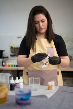 Odaklanmış zanaatkar fitili el yapımı mumu için hazırlıyor. Stüdyosunda renkli boyalar ve aletlerle çevrili.