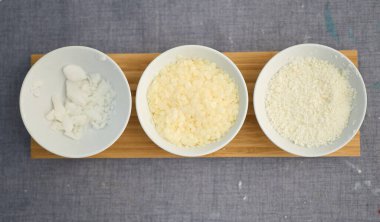 İçinde muhtelif balmumu formları bulunan üç beyaz kase, mum yapımına hazır ahşap bir tepside oturur.
