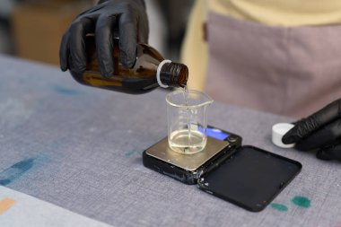 Bir mum imalatçısı dikkatlice eritilmiş balmumunu dijital ölçekte yerleştirerek bir stüdyoda el yapımı mumlar için malzemeler hazırlıyor.