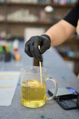 Eldivenli eldiven yakın plan, erimiş balmumunu ahşap bir sopayla karıştırıyor, canlı bir el sanatları stüdyosunda mum yapımına hazırlanıyor.