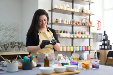 Kadın esnaf, renkli atölyesinde, aletler ve malzemelerle çevrili el yapımı mumlar yapmak için balmumu çarşaflar hazırlıyor.