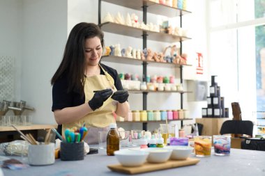 Kadın sanatçı, alet ve malzemelerle dolu canlı bir atölyede el yapımı mumlar yapmak için renkli balmumu çarşaflar hazırlıyor.