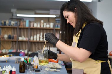 Konsantre olmuş usta kadın sıcak balmumunu ahşap sopayla karıştırıyor, kavanozlara dökmeye hazırlanıyor ve renkli atölyesinde el yapımı mumlar yapıyor.