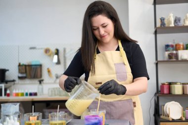 Renkli atölyesinde el yapımı mumlar yaparken konsantre bir kadın erimiş balmumunu cama döküyor.