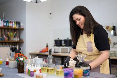 Önlük ve eldiven giyen kadın atölyesinde el yapımı mumlar yapmak için renkli balmumu ve aletler hazırlıyor.
