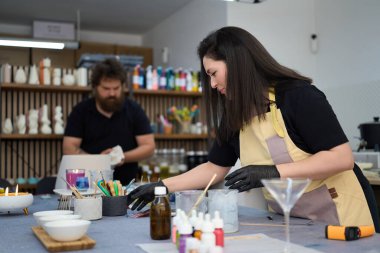 Kadın sanatçı, parlak zanaat atölyesinde el yapımı mumlar yapmak için renkli balmumu ve aletleri dikkatlice hazırlıyor.
