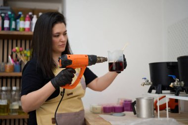 Isı tabancasıyla balmumu ısıtan usta kadın renkli stüdyosunda el yapımı mumlar yapmaya hazırlanıyor.