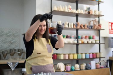 Gülümseyen zanaatkar, canlı zanaat atölyesinde sıcak balmumu karıştırıyor, renkli malzemelerle çevrili eşsiz el yapımı mumlar yaratıyor.