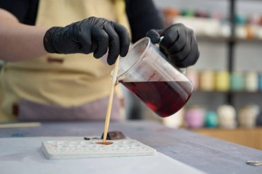 Zanaatkâr ellerin kalp şeklindeki kalıba erimiş kırmızı mum dökerek el yapımı mumları sanat atölyesinde oluşturduğu yakın plan.