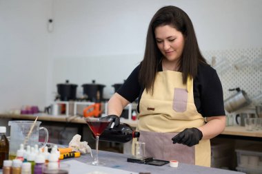 Zanaatkar kadın canlı ve renkli bir stüdyo ortamında ustalıkla el yapımı mumlar üreterek bir deney şişesine canlı kırmızı mum döküyor.