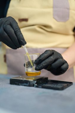 Bir mum imalatçısının yakın plan çekimleri, eritilmiş balmumuna özenle parfüm yağı ekleyerek, mum yapımında kullanılan hassasiyeti ve sanatsal beceriyi gösteriyor.