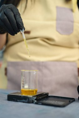 Bir mum imalatçısı dikkatlice pipet kullanarak bir beher yağına parfüm katar ve titizlikle el yapımı mumlar yakar.