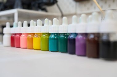 Renkli pigmentlerle dolu küçük şişeler gökkuşağı gradyanı ile düzenlenmiş, bir el sanatları stüdyosunda mum yapımına hazır.