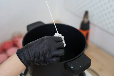 Eldivenli eller dikkatle fitili sıcak, erimiş balmumuna batırıyor, yaratıcılıkla dolu samimi bir atölyede el yapımı mumlar yaratıyor.