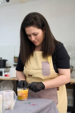 Konsantre olmuş usta kadın parlak atölyesindeki renkli el yapımı muma son rötuşları ekliyor.