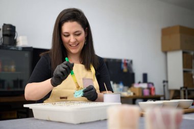 Gülümseyen kadın fırça ve balmumu sürüyor, yaratıcı enerjiyle dolu renkli bir atölyede eşsiz mumlar yapıyor.