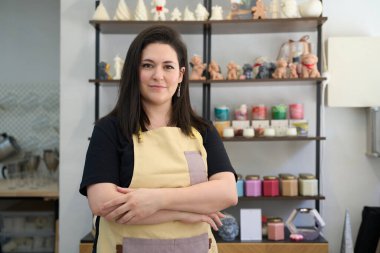 El yapımı mumlar ve malzemelerle çevrili renkli atölyesinde gururla duran kendinden emin bir kadın girişimcinin portresi.