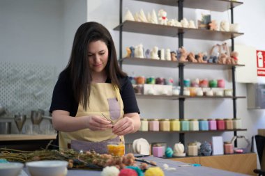 Renkli atölyede el yapımı muma dekoratif kurutulmuş çiçekler ekleyen konsantre bir zanaatkar kadın.