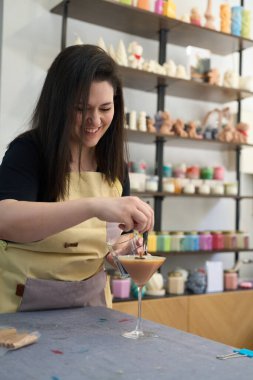 Gülümseyen bir zanaatkar atölyesinde mum şeklinde bir kokteyl bardağı hazırlıyor.