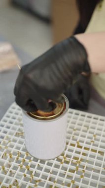 Eldivenli eller ustalıkla bir konteynıra balmumu döker, canlı bir zanaat atölyesinde el yapımı mum yapımının titiz sürecini gözler önüne serer.