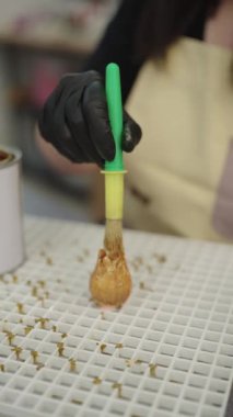 Yetenekli bir zanaatkar, gül şeklindeki narin mumu altın renginde boyuyor, parlak yaratıcı çalışma alanının içinde karmaşık bir zanaat sergiliyor.