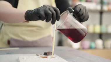 Mum imalatçısı kalp şeklinde bir kalıba kırmızı mum dökerek renkli bir sanat stüdyosunda el yapımı mumlar yaratıyor.