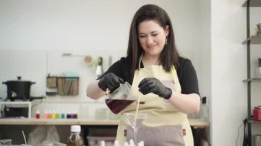 Zanaatkar, renkli stüdyosunda el yapımı mumlar yaparak, martini bardağına erimiş kırmızı mum döküyor.