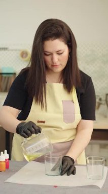 Becerikli kadın sanatçı, atölyesinde el yapımı mumlar yaparken cam kavanoza dikkatlice erimiş balmumu dökerek hassas ve yaratıcı bir süreç sergiliyor.