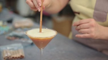 Bir kadın martini bardaklarına ahşap fitil yerleştiriyor mum dolu, eşsiz ve dekoratif mumlar yaratıyor.