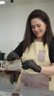 Profesyonel bir zanaatkar atölyesinde el yapımı mum üretimi sırasında cam kaplara erimiş balmumu dökerek dikkatle çalışır.