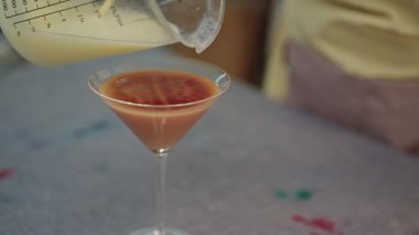 Krema kadehten yavaşça kırmızı alkollü bir içecek içeren bir martini bardağına dökülüyor.