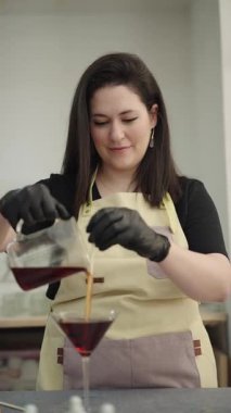 Sanatçı kadın, atölyesinde el yapımı mumlar yapmak için martini bardağına kırmızı balmumu karıştırıyor.